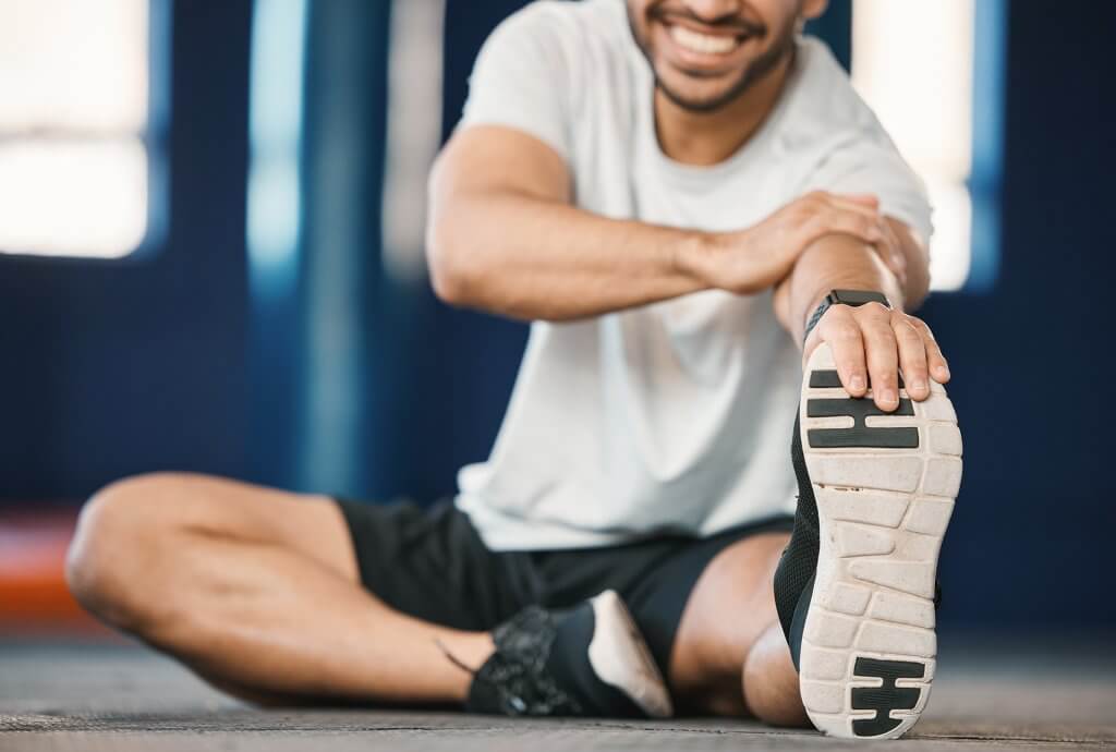 direct shot of a male athlete stretching and holding his foot and smiling.