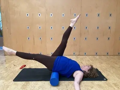Personal Trainer Dana balancing on a foam roller with one leg extended to the sky and another parallel