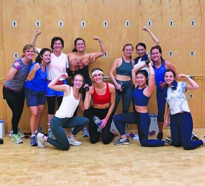 A group of women smiling and showing their biceps after a bachelorette party workout. 